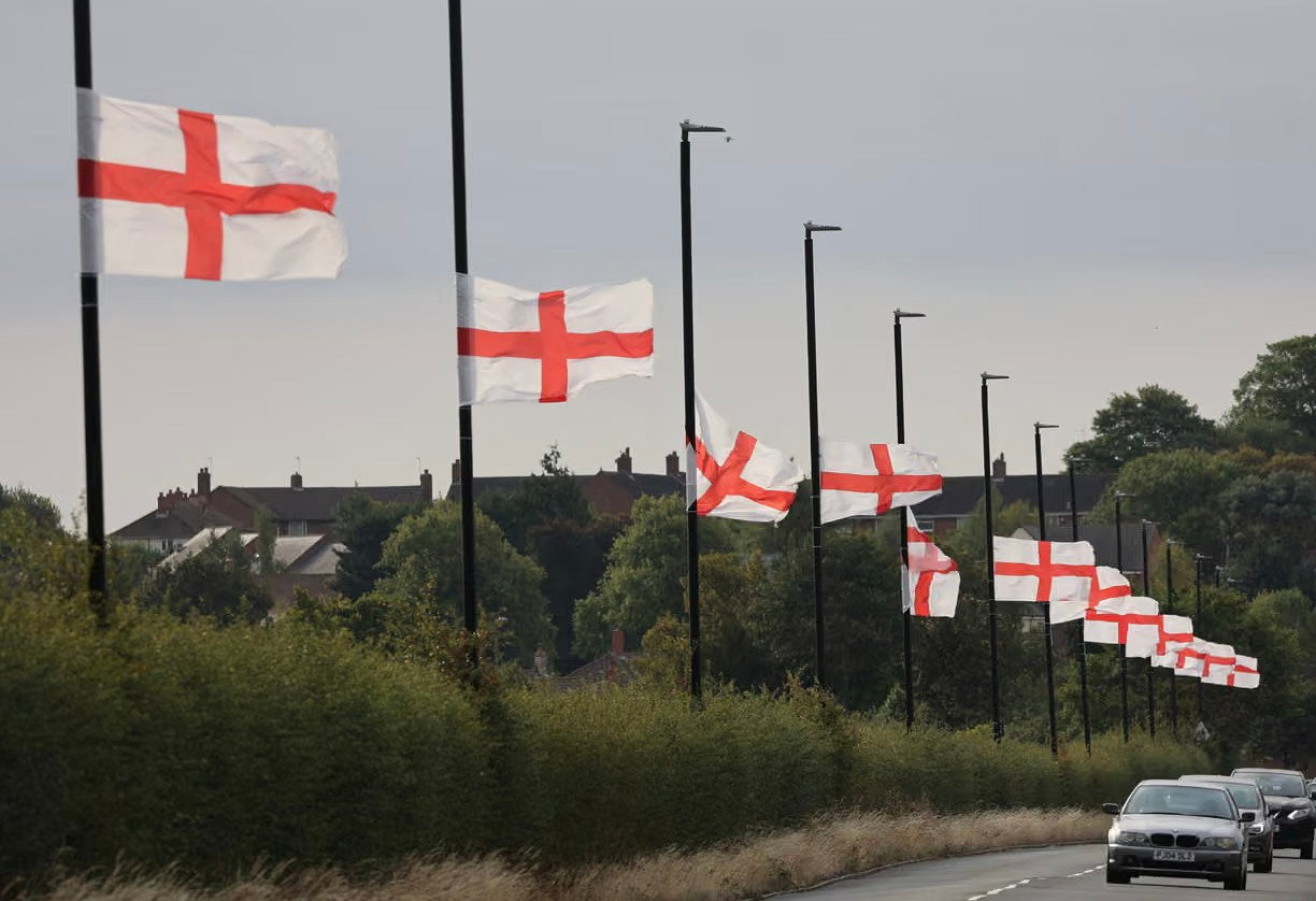 Row of English flags along a road with cars passing by