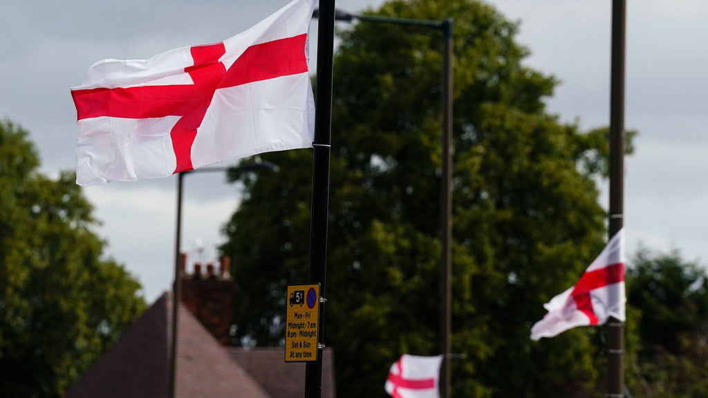 English flags waving against a backdrop of trees and a building.