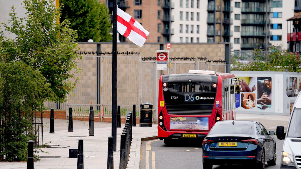 Red bus on a city street with a flag and buildings in the background