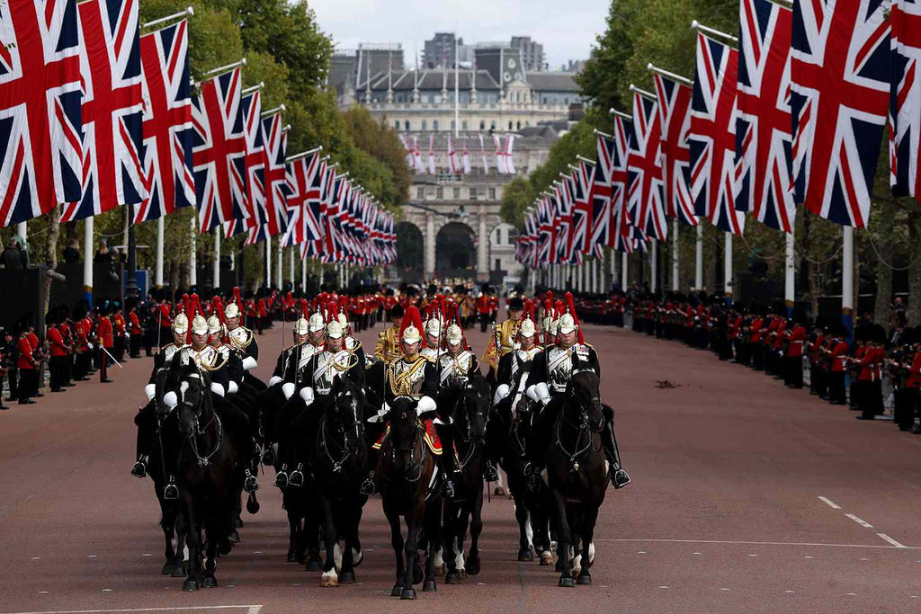 Formal procession with horses and uniformed riders in London, featuring British flags.